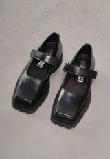 Zapato tipo guillermina de cuero negro con punta cuadrada, tira con hebilla sobre el empeine y suela track.