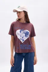 Remera de manga corta color marrón oscuro con efecto gastado, corte holgado y estampado frontal de Minnie Mouse dentro de un corazón blanco con texto en azul.
