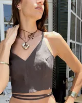 Collar con dije dorado irregular con agujero central, colgando de cordón negro ajustable.