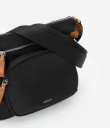 Bandolera negra de poliéster con detalles en cuero sintético color marrón. Tiene correa transversal ajustable, cierre de cremallera, bolsillos delanteros y placa metálica con el logo de la marca.