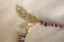 Gargantilla con cinta de tela estampada en tonos marrón y blanco, con dije dorado en forma de gota.