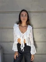 Blusa de encaje blanco con volados en el escote y mangas acampanadas. Se ata en el frente con lazos.