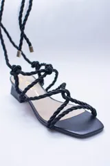 Sandalias doradas con tiras de cuerda para atar al tobillo.