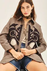 Campera manga larga color marrón con cuello camisero, confeccionada en gabardina con parches bordados en delantero y espalda.