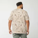 Camiseta de manga corta color beige con estampado de hojas en tonos blanco y marrón.