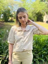 Camisa color beige de mangas cortas abullonadas y cuello con puntilla bordada. Cierre frontal con botones.