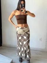 Pollera larga de tiro bajo con estampado geométrico en tonos marrón y blanco. Se ajusta a la cintura con un cinturón ancho de cuero sintético color beige con tachas doradas.