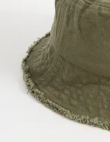 Piluso verde militar de denim con ala corta y bordado de un trébol de cuatro hojas en color rosa. El borde del ala está desflecado.