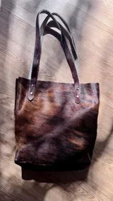 Bolso tipo tote de cuero con pelo color marrón y blanco, con manijas de cuero crudo.