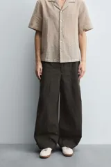 Pantalón cargo de corte ancho y relajado, color verde oscuro o negro, con cintura elástica, bolsillos laterales de parche y bolsillos traseros de vivo. Presenta pliegues verticales marcados en la parte delantera y cordones ajustables en los bajos.