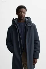 Parka azul marino de tejido técnico repelente al agua, corte regular fit, interior acolchado, cuello alto con capucha, mangas largas con puños de rib, cuello interior desmontable con cremallera, bolsillos de vivo en cadera y bolsillo interior. Cierre frontal con cremallera oculta por solapa con botones a presión.