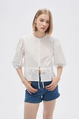 Blusa blanca de algodón con textura de lunares, corte recto, cuello redondo, mangas 3/4 abullonadas y cierre frontal con botones.