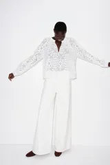 Blusa blanca de algodón con broderie, corte holgado, cuello mao con frunces, abertura en V y mangas globo largas con puños abotonados.