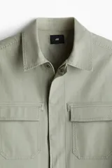 Sobrecamisa verde oliva de corte recto, con cuello inglés, cierre frontal con botones a presión y dos bolsillos de parche con solapa en el pecho.