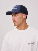 Gorra azul marino con visera, de lona de algodón y malla trasera. Estampado frontal con el logo de la marca Rusty.