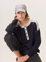 Buzo de manga larga con diseño de bloques de color y textura. El cuerpo principal es marrón, la espalda superior y hombros tienen un panel de tejido a rayas grises y azules, y los hombros superiores son de color beige rosado. Presenta costuras decorativas en rojo que separan los bloques de color.