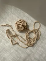Gargantilla beige tejida a crochet con forma de flor y tiras para atar.