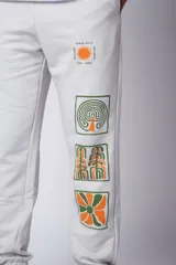 Pantalón de jogging gris claro con puños elásticos, cintura con cordón ajustable y estampado con motivos geométricos en la pierna izquierda.