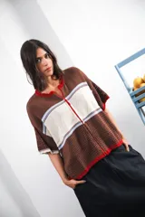 Remera de tejido calado color crudo con rayas horizontales rojas y terminaciones marrones, con cierre frontal y logo bordado.