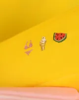 Neceser naranja de tela con cierre superior y logo de la marca en etiqueta negra. Presenta bordados de emojis: copa de vino, fuegos artificiales y mano verde.