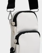 Bandolera color crudo con detalles en negro, correa ancha regulable y bolsillo frontal.