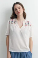 Blusa blanca de manga corta con escote en V y bordados florales en los hombros.