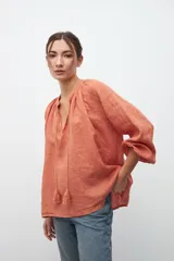 Camisa color ocre de crepe con escote en V con cordones y borlas, mangas largas abullonadas con puños elásticos.