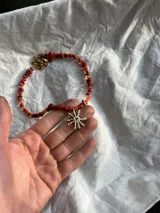 Collar de piedras de color naranja y dije de sol plateado. Las piedras son de diferentes tamaños y formas. El dije de sol es de bronce y tiene un diámetro de 2.5 cm.