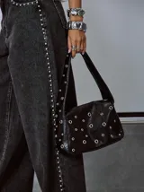 Bolso tipo baguette negro con textura de cuero y múltiples ojales metálicos.