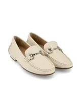Mocasín de cuero color crema con detalle de hebilla metálica plateada.