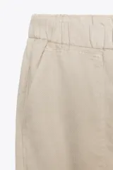 Pantalón color beige de tiro medio con cintura elástica ajustable con cordones, bolsillos delanteros y falsos bolsillos de vivo en la espalda. El bajo es ajustable con botón a presión.