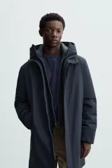 Parka azul marino de corte recto, con capucha y cuello alto desmontable. Interior acolchado, cierre frontal con cremallera oculta y botones a presión, bolsillos laterales y puños de rib.