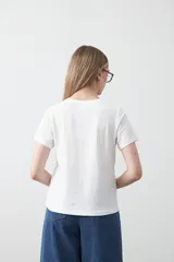 Remera blanca de manga corta con cuello redondo y bordado floral en relieve de color beige claro en el frente.