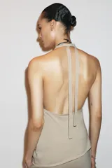 Top color beige confeccionado en algodón 100% con efecto teñido. Presenta cuello halter con lazada y escote drapeado. El bajo tiene un acabado asimétrico.