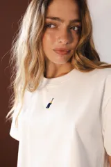 Remera blanca de algodón con cuello redondo y manga corta. Presenta un pequeño bordado de un pato en el pecho.