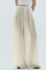 Pantalón palazzo color crudo, de tiro alto, confeccionado en lyocell. Presenta bolsillos laterales ocultos, detalle de pliegues en el delantero y cierre frontal con cremallera y botones.