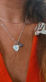 Conjunto de collar y dije de plata 925. El collar es de cadena de eslabones plateada y el dije es un corazón con la inscripción "Fifole" y un dije de ojo turco.