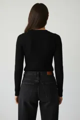 Sweater de tejido de punto color crema, con cuello redondo a la base y tres botones decorativos en el hombro izquierdo.