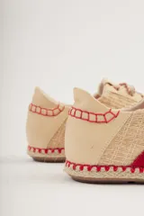 Championes de cuero color beige con detalles en rojo, suela de yute y cordones con diseño trenzado.