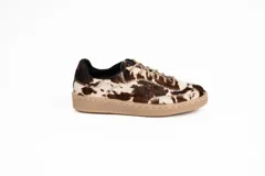 Zapatillas bajas con capellada de pelo de vaca color marrón y blanco, con cordones finos color beige y suela de goma color beige.