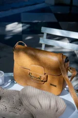 Bandolera color beige con textura símil reptil, cierre con broche metálico dorado y correa larga regulable.