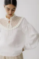 Blusa color ladrillo con cuello alto de crochet y lazos para ajustar. Mangas largas abullonadas con puños elásticos.