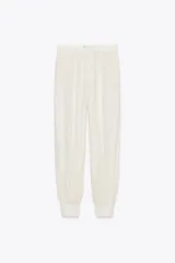 Pantalón de tiro medio color crudo con rayas verticales, confeccionado en hilatura con lino. Tiene bolsillos laterales ocultos en costura y de vivo en espalda, detalle de pliegues y bajo acabado en puño.
