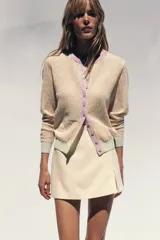 Chaqueta de punto color marrón con cuello redondo y manga larga. Presenta detalle de color azul en cuello, puños y ruedo. Cierre frontal con botones color celeste.