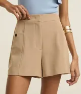 Short color beige de cintura alta, confeccionado en tejido plano con estructura sastre, con bolsillos laterales con tachuelas metalizadas.