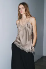 Top lencero de color marrón oscuro, con escote pico y tirantes finos. Presenta detalles de encaje a tono en el escote y en el bajo asimétrico.