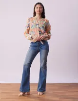 Blusa de gasa estampada a rayas verticales en tonos celeste, lila, naranja y marrón. Tiene cuello a la base con escote en V y botones. Delantera con bolsillo aplicado. Largo de manga regulable con presilla y botón. Terminación anudada opcional.