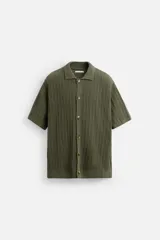 Camisa verde militar de punto con estructura abierta, corte regular fit, cuello solapa, manga corta y cierre frontal con botones.