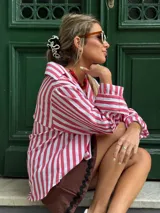 Camisa oversize a rayas verticales rojas y blancas, de algodón, con cuello camisero, mangas largas con puños abotonados y bolsillo en el pecho.