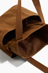 Bolso shopper marrón de lona de algodón con doble asa de mano y múltiples compartimentos exteriores, tres en los lados largos y uno de malla en los laterales.